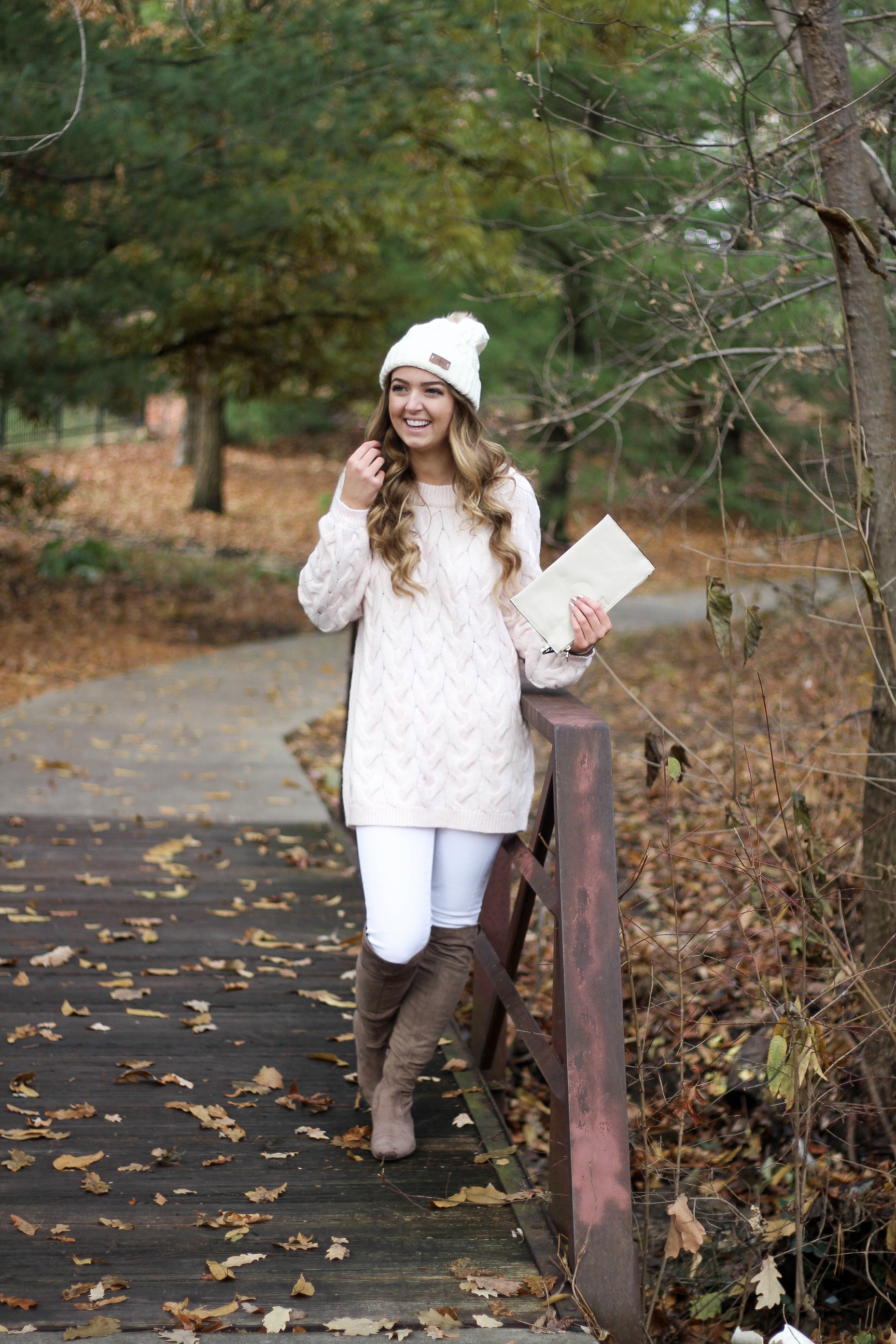 Pink cable knit sweater with white jeans and over the knee tan suede boots topped with an adorable faux fur beanie! The perfect winter outfit by Lauren Lindmark on dailydoseofcharm.com daily dose of charm