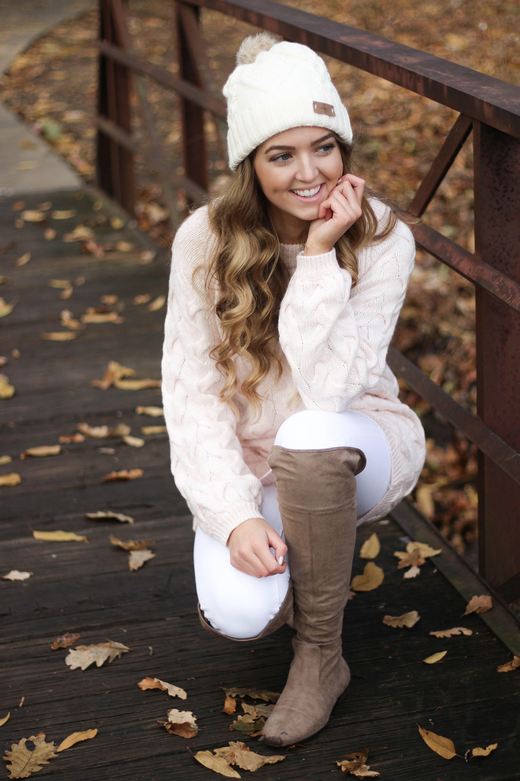 Pink cable knit sweater with white jeans and over the knee tan suede boots topped with an adorable faux fur beanie! The perfect winter outfit by Lauren Lindmark on dailydoseofcharm.com daily dose of charm