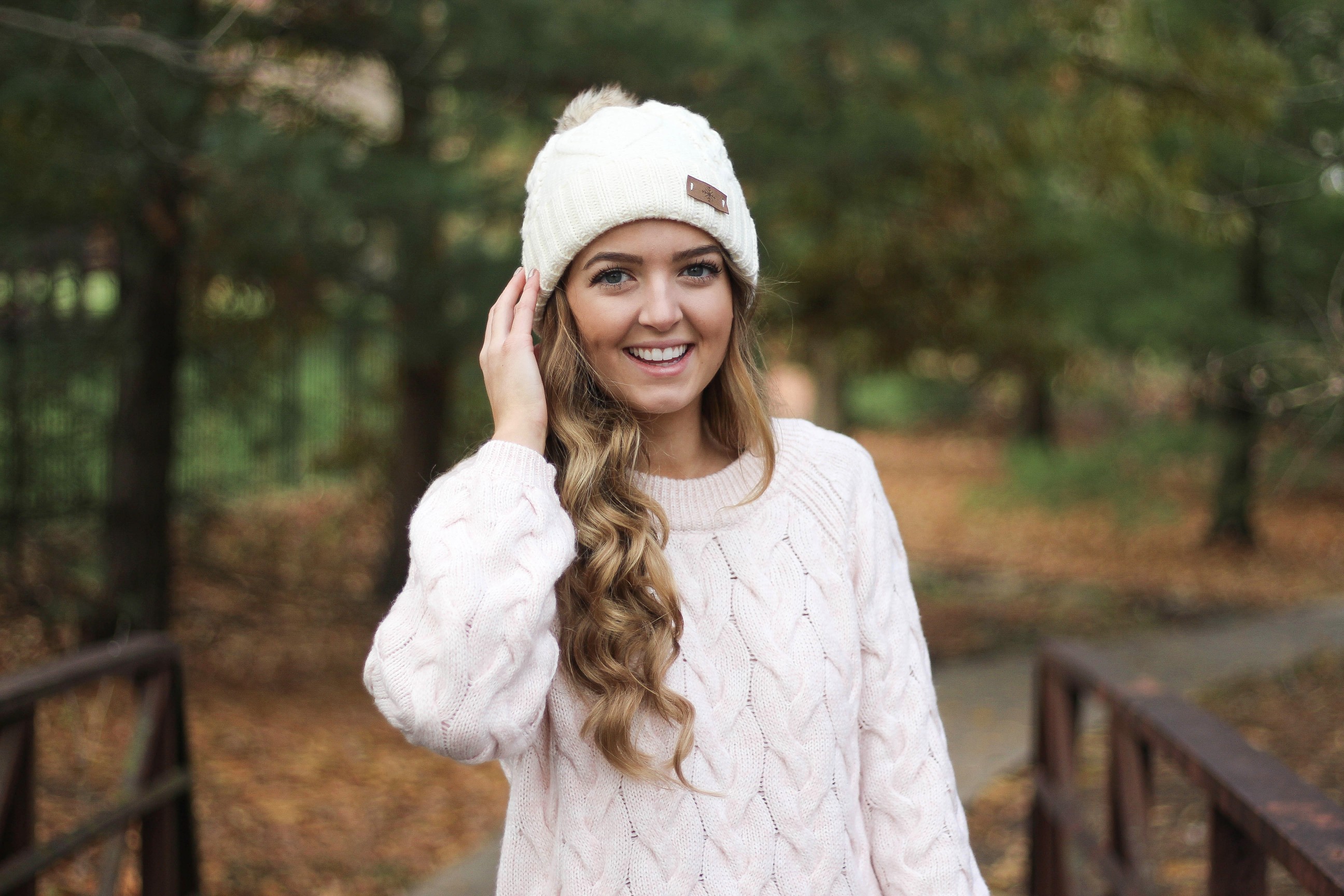 Pink cable knit sweater with white jeans and over the knee tan suede boots topped with an adorable faux fur beanie! The perfect winter outfit by Lauren Lindmark on dailydoseofcharm.com daily dose of charm