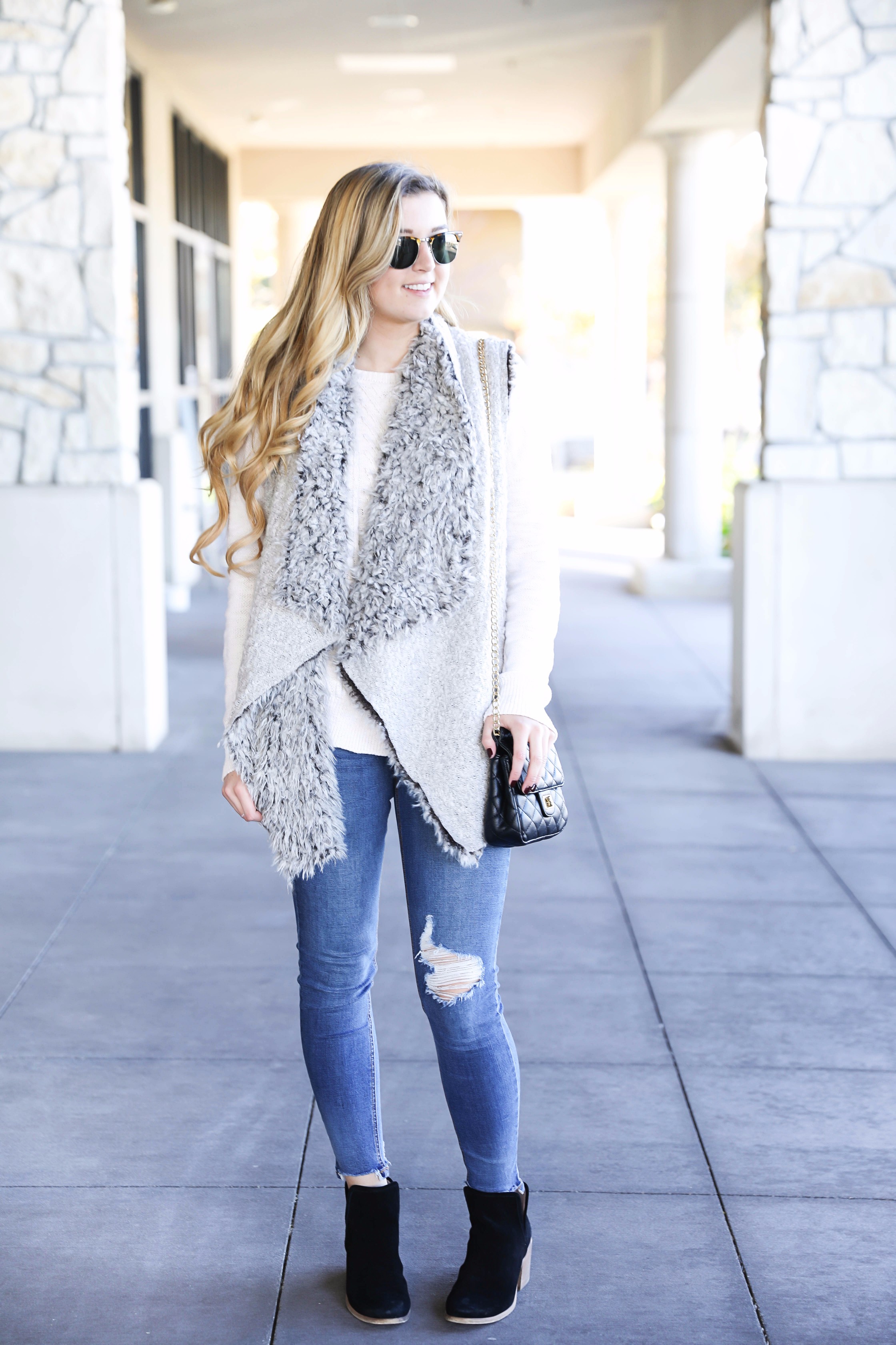 Fuzzy vest with cable knit sweater! Paired with my favorite ripped jeans and clubmaster sunglasses. These black booties are the best! Details on fashion blog daily dose of charm by lauren lindmark