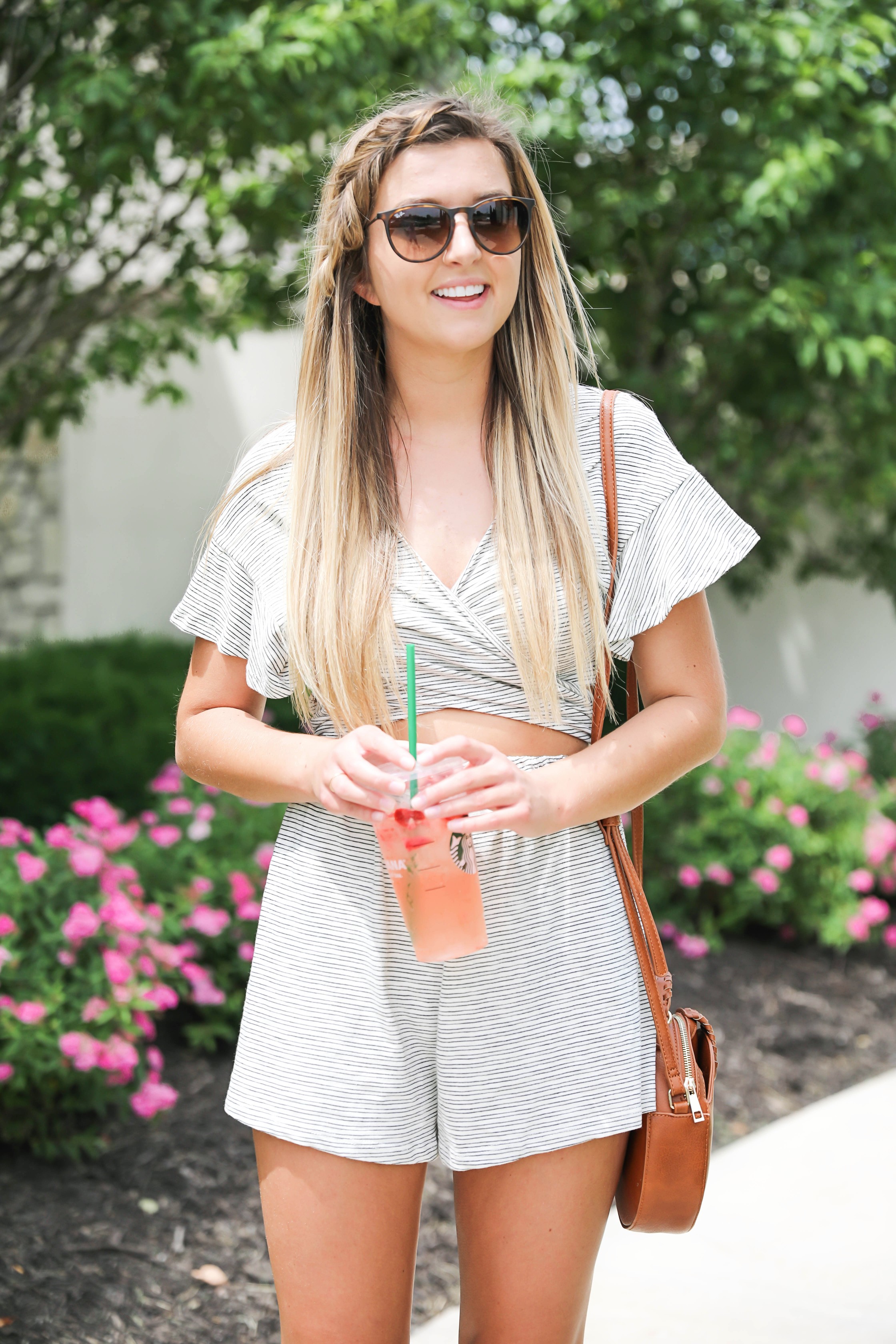 Striped tied romper with cute ruffle sleeves! Only $45! Photoshoot with spring pink flower bushes! I braided my bangs into a fishtail braid! I finished the look with a Sole Society bag and my tory burch miller sandals! Such a cute summer outfit on fashion blog daily dose of charm by lauren lindmark