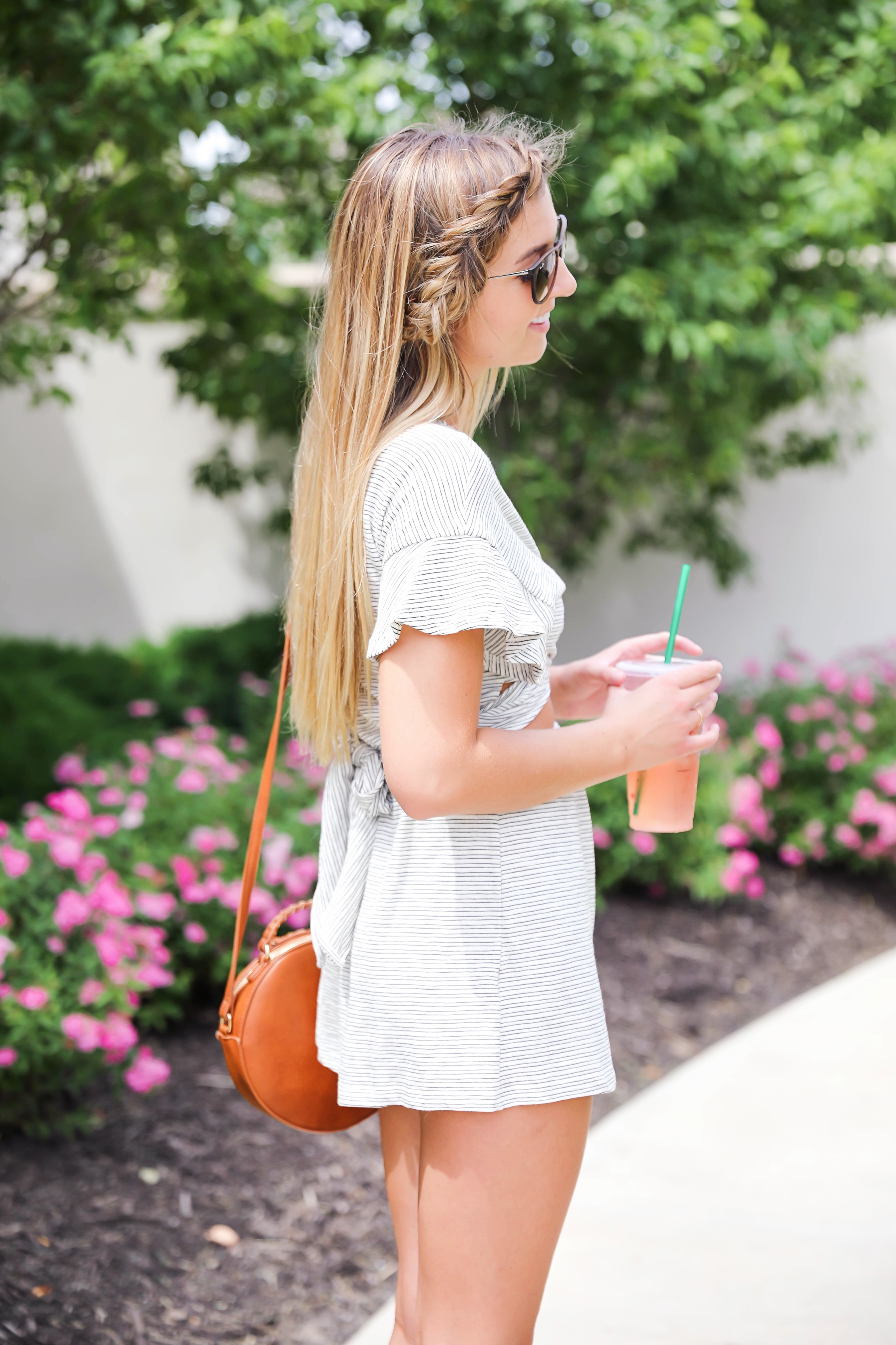 Striped tied romper with cute ruffle sleeves! Only $45! Photoshoot with spring pink flower bushes! I braided my bangs into a fishtail braid! I finished the look with a Sole Society bag and my tory burch miller sandals! Such a cute summer outfit on fashion blog daily dose of charm by lauren lindmark