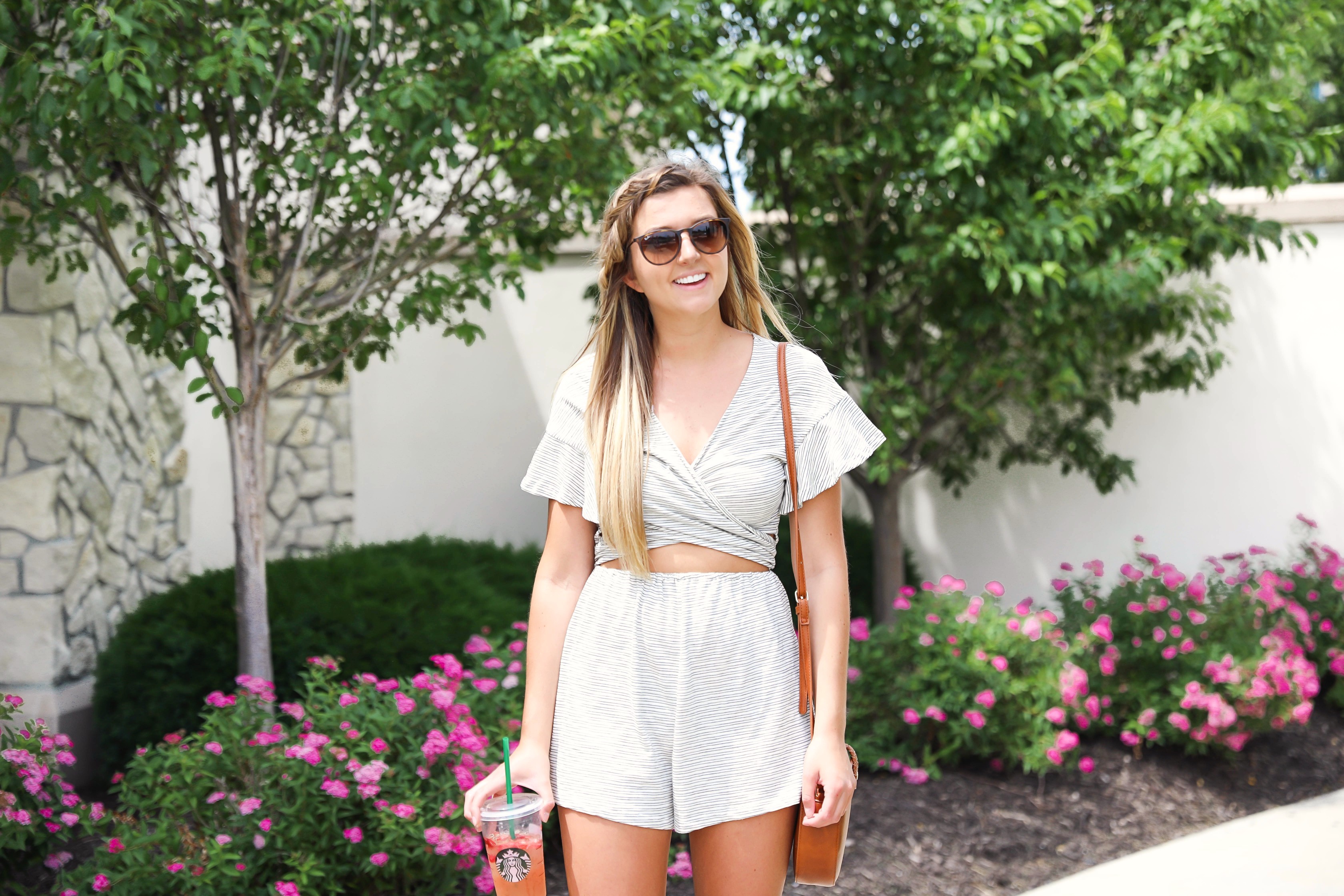 Striped tied romper with cute ruffle sleeves! Only $45! Photoshoot with spring pink flower bushes! I braided my bangs into a fishtail braid! I finished the look with a Sole Society bag and my tory burch miller sandals! Such a cute summer outfit on fashion blog daily dose of charm by lauren lindmark