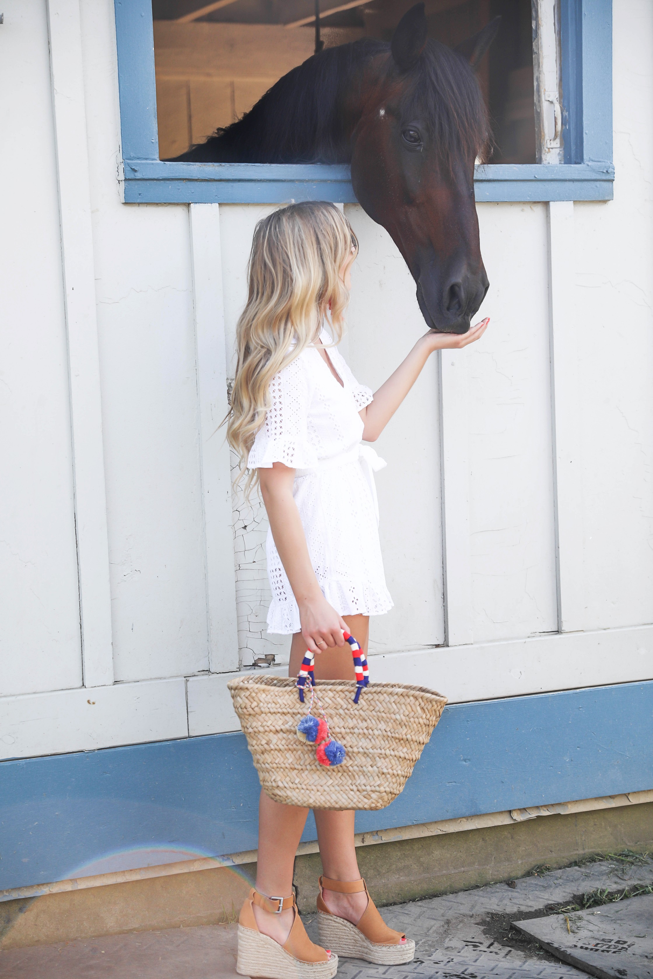 White ruffle tied romper perfect for dressing up or dressing down! Paired with a cute straw beach bag for fourth of july! The beach bag has red white and blue pom poms on it! I finished the fourth of july outfit with red tassel earrings and my favorite wedges! Details on fashion blog daily dose of charm by lauren lindmark