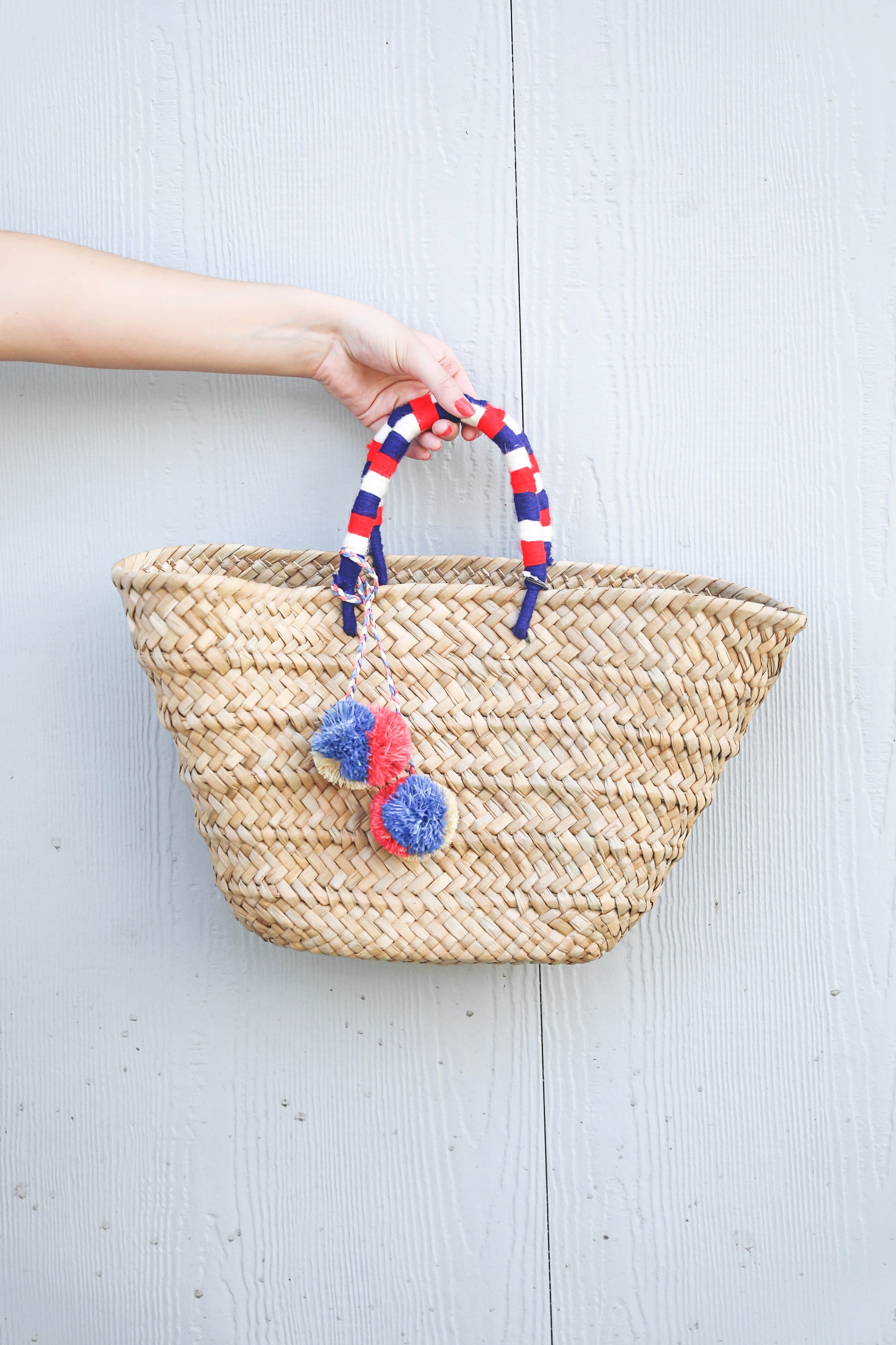 White ruffle tied romper perfect for dressing up or dressing down! Paired with a cute straw beach bag for fourth of july! The beach bag has red white and blue pom poms on it! I finished the fourth of july outfit with red tassel earrings and my favorite wedges! Details on fashion blog daily dose of charm by lauren lindmark