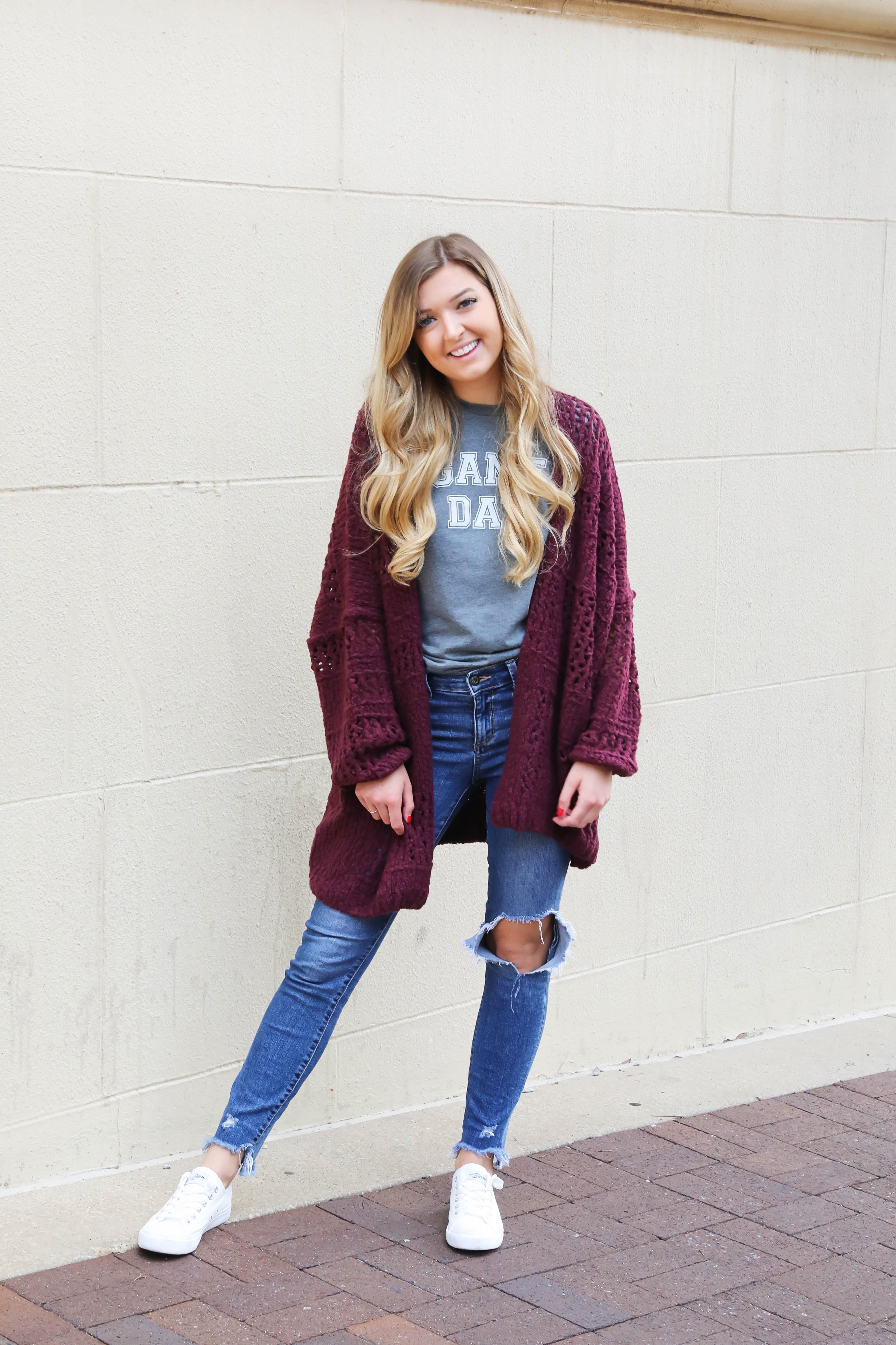 Free People Burgundy cardigan paired with a cute gray game day tshirt! These ripped denim jeans are so perfect for fall and I love these inexpensive white sneakers with the look! This is a perfect game day outfit for football games this fall! Details on daily dose of charm by lauren lindmark