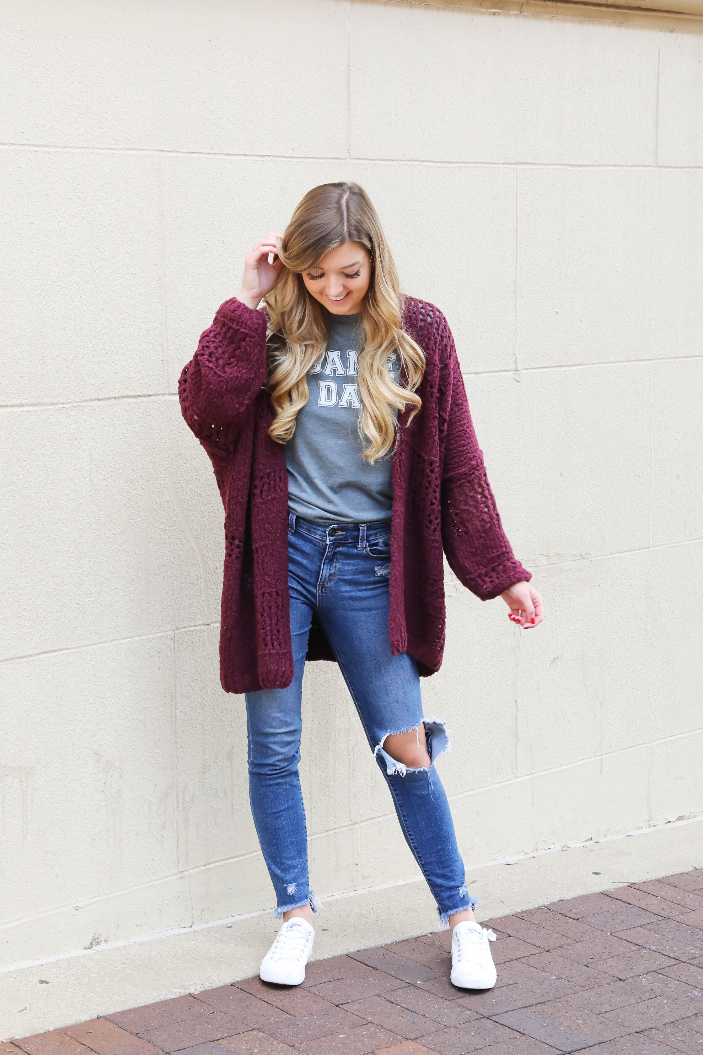 Free People Burgundy cardigan paired with a cute gray game day tshirt! These ripped denim jeans are so perfect for fall and I love these inexpensive white sneakers with the look! This is a perfect game day outfit for football games this fall! Details on daily dose of charm by lauren lindmark