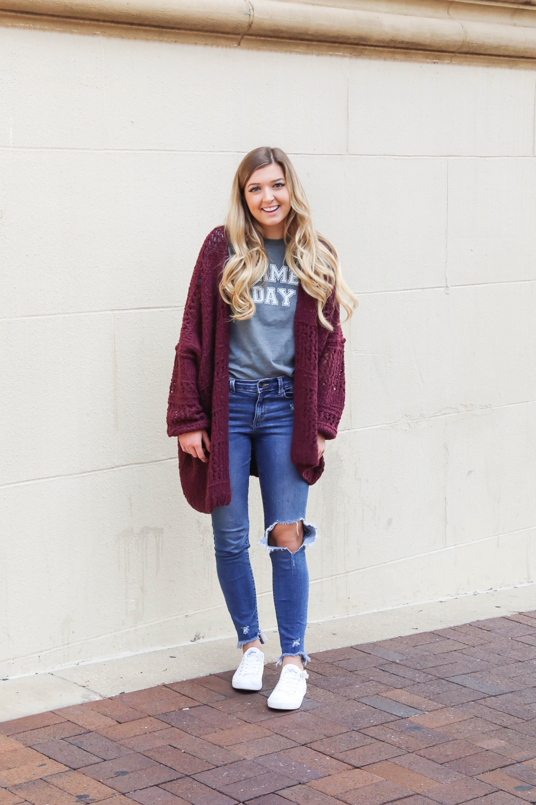 Free People Burgundy cardigan paired with a cute gray game day tshirt! These ripped denim jeans are so perfect for fall and I love these inexpensive white sneakers with the look! This is a perfect game day outfit for football games this fall! Details on daily dose of charm by lauren lindmark