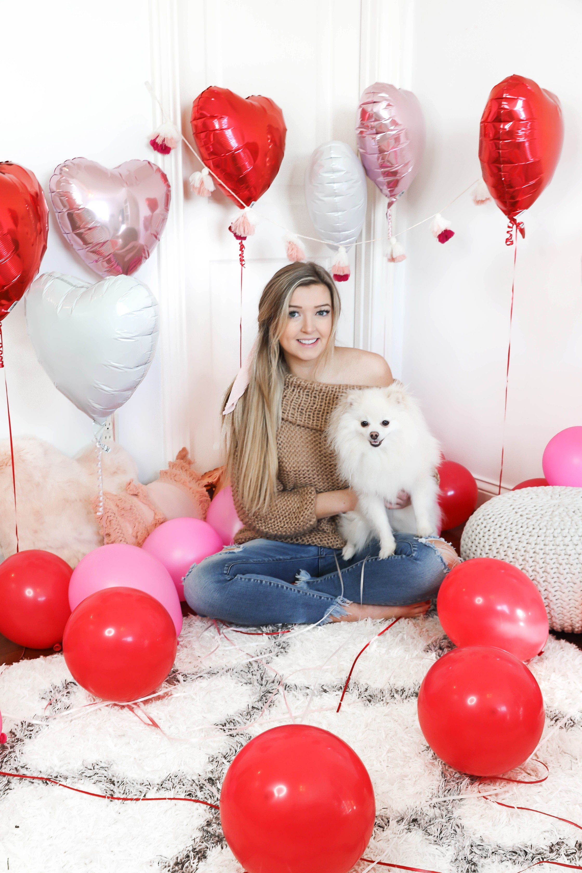 Valentine's Day shoot with the cutest heart shaped balloons and pink and red decor! My cute little pomeranian puppy dog made an appearance in the pics! I am wearing the cutest, tan, off the shoulder sweater from amazon and the cutest ripped denim from Red Dress Boutique! Details on style and fashion blog daily dose of charm by lauren lindmark