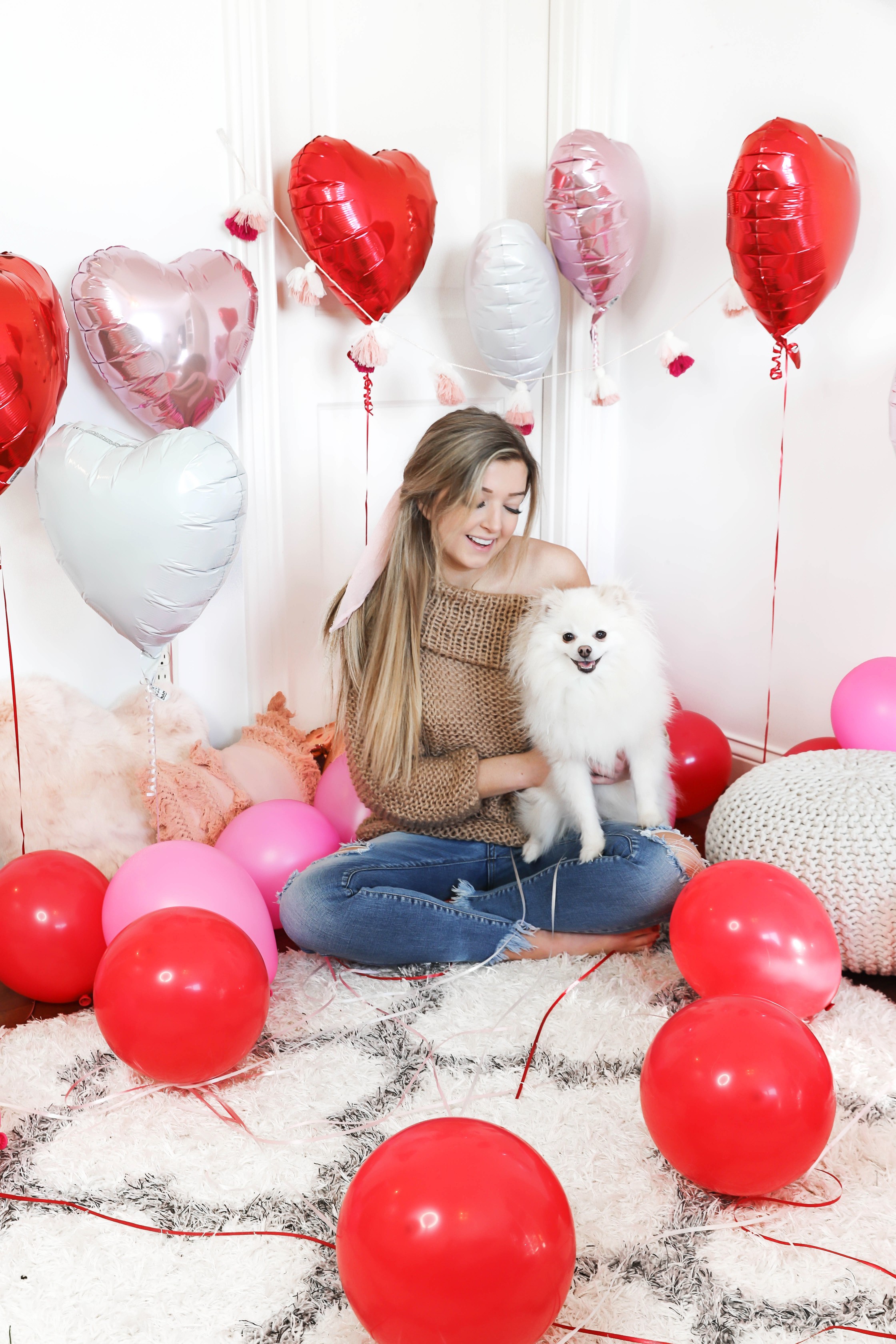 Valentine's Day shoot with the cutest heart shaped balloons and pink and red decor! My cute little pomeranian puppy dog made an appearance in the pics! I am wearing the cutest, tan, off the shoulder sweater from amazon and the cutest ripped denim from Red Dress Boutique! Details on style and fashion blog daily dose of charm by lauren lindmark